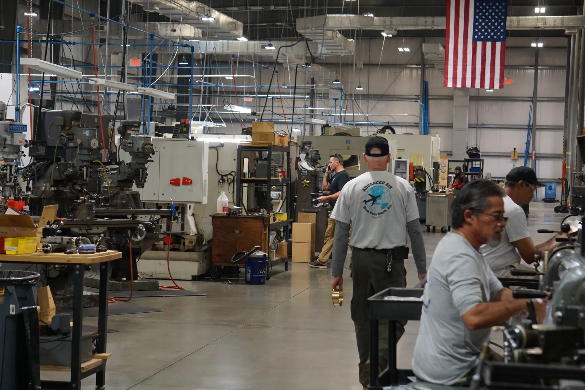 Manual lathes and mills under an American flag on the Advanced Air shop floor